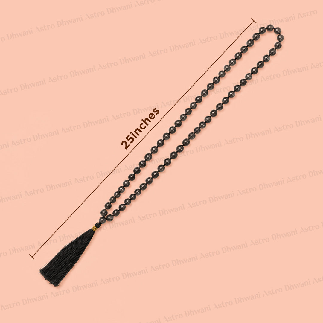 Black beaded mala prayer necklace with a black tassel and gold accent, shown on a peach background with a 25 inches length measurement overlay.