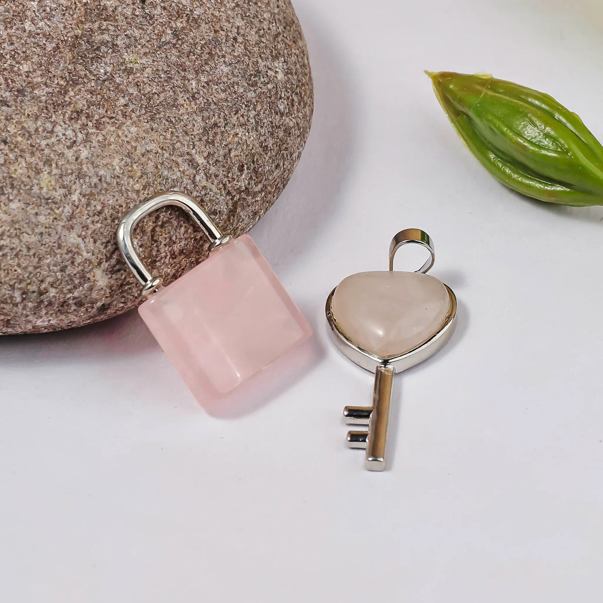 Pink ceramic lock and silver key-shaped charm on a light surface with a stone and leaf in the background.