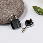 Black padlock and key on a white surface with a stone and leaf in the background