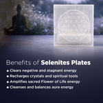 Selenite plate with a Flower of Life design on a dark surface, with a person meditating in the background.
