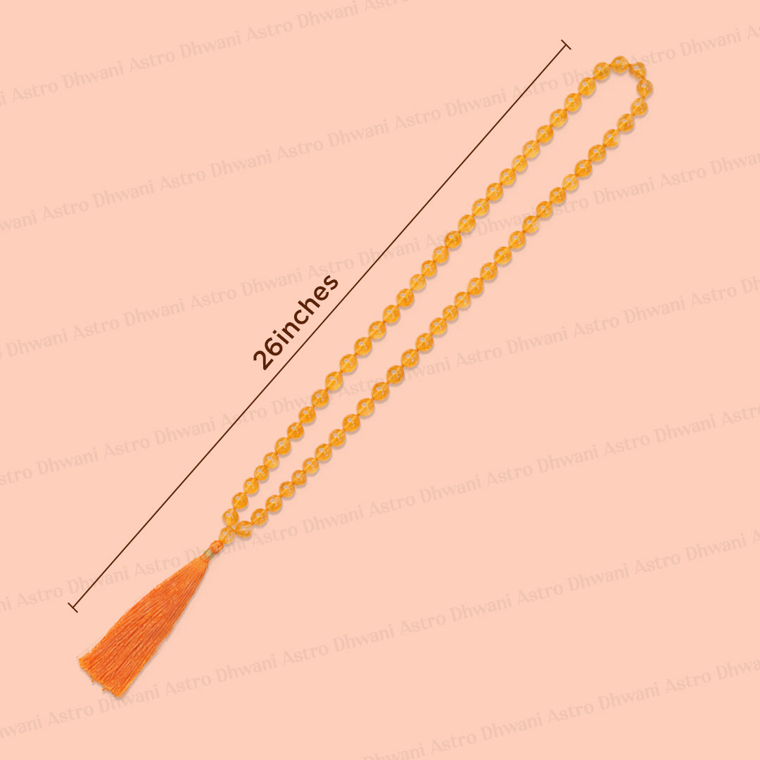 An orange beaded necklace or prayer bead strand with a tassel, shown diagonally on a peach background with a measurement line indicating 26 inches.Natural Yellow Citrine Ganth Mala | Prosperity & Abundance Mala | Handknotted Japa Mala for Meditation, Puja & Spiritual Practice
