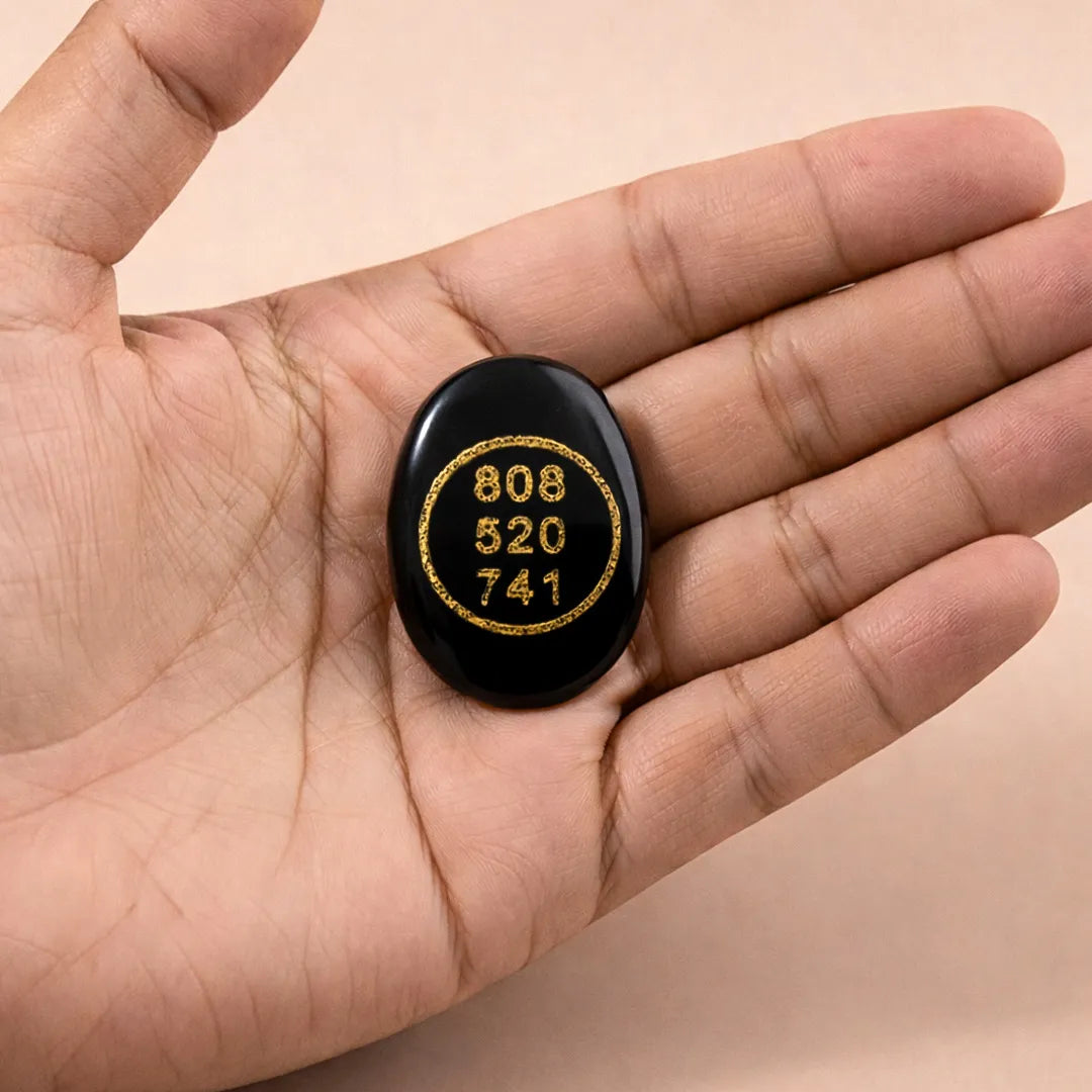 Black stone with gold text held in a hand against a beige background