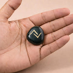 Black stone with gold symbol held in a hand against a beige background