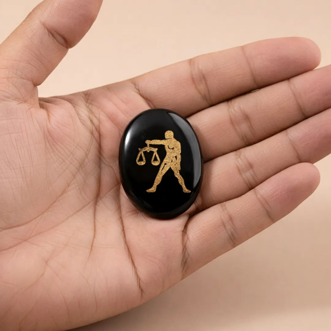 Hand holding a black stone with a gold Libra zodiac symbol on a beige backgroundLibra Zodiac Sign Coin – Abhimantrit Astrology Coin for Balance & Relationships