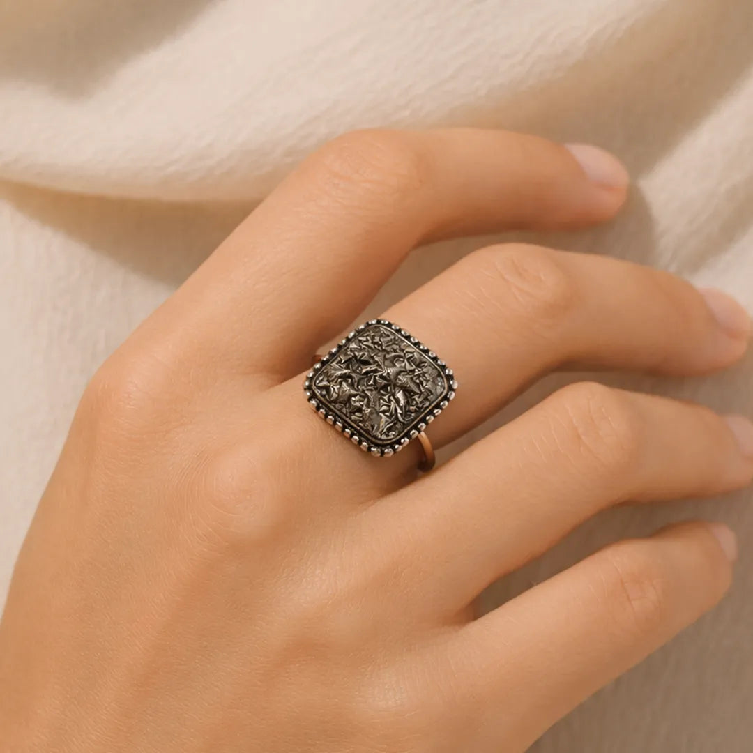 Hand wearing a decorative ring on a neutral background