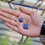 Hand holding a small heart-shaped key and blue padlock against a blurred outdoor background