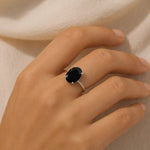 Hand wearing a ring with a dark gemstone on a neutral background