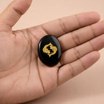 Black stone with a gold emblem held in a hand against a beige background