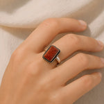 Hand wearing a ring with a brown stone on a neutral background