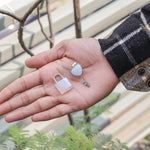 Hand holding a small lock and key with a blurred outdoor background