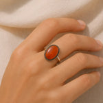 Hand wearing a ring with an orange stone on a beige background