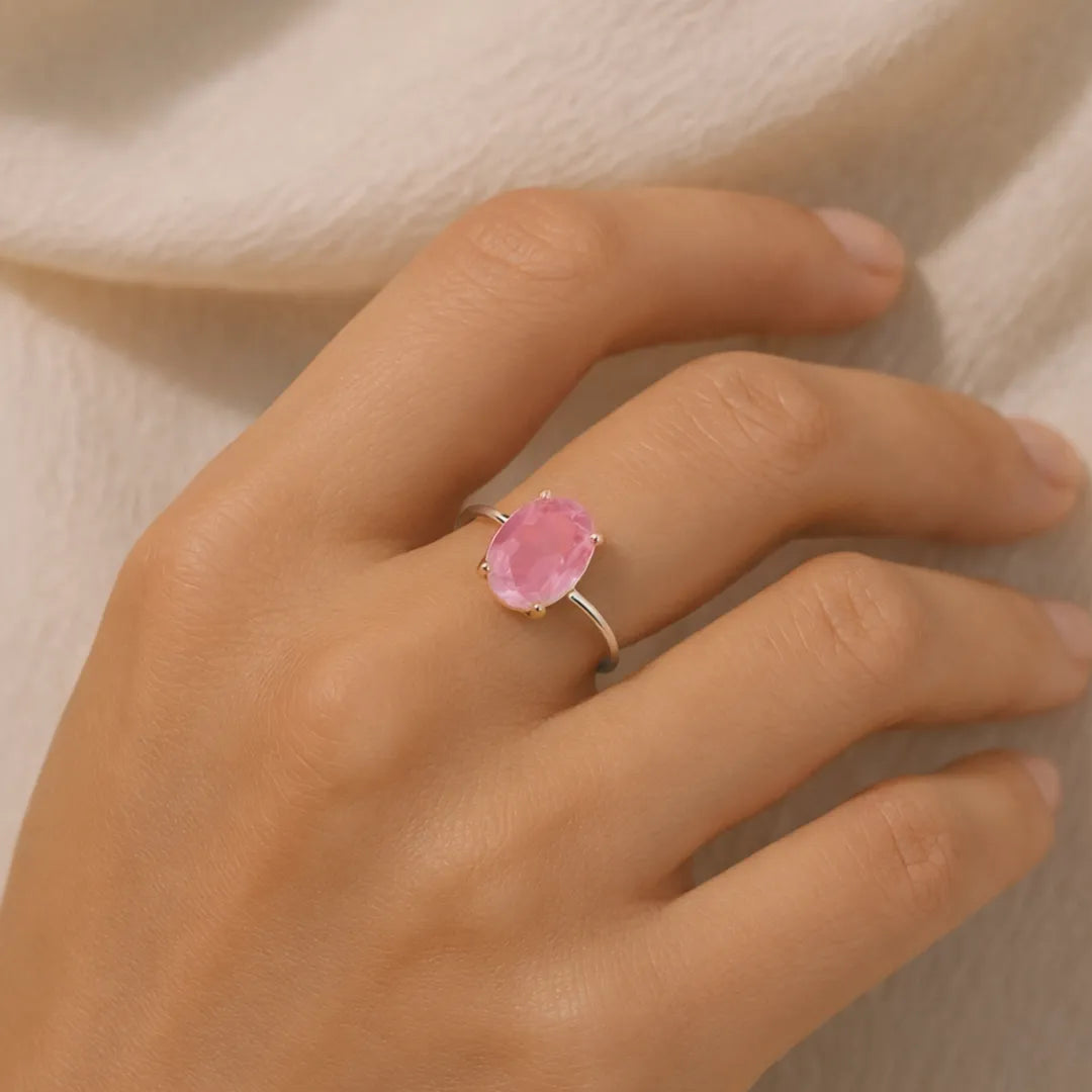 Hand wearing a ring with a pink gemstone on a neutral background