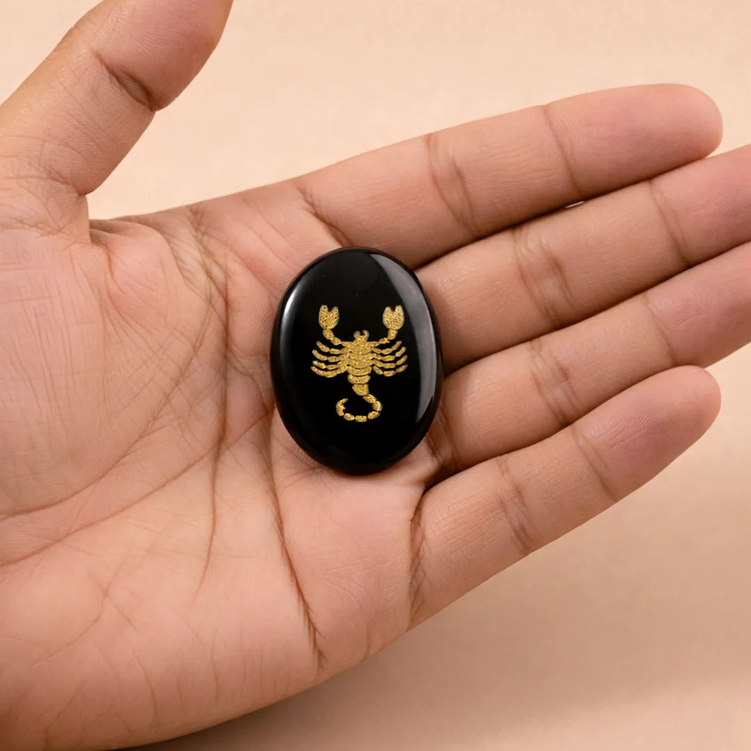 Black stone with gold scorpion design held in a hand against a beige background