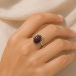 Hand wearing a ring with a red gemstone on a neutral background