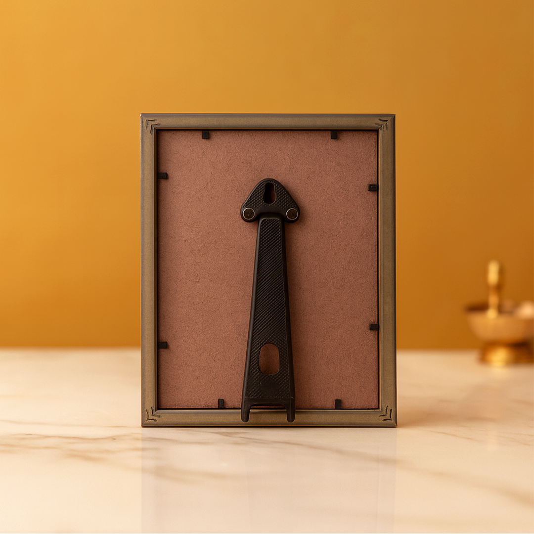 Decorative metal object on a cardboard backing in a gold frame against an orange wall.