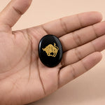 Black stone with a gold bull emblem held in a hand against a beige background