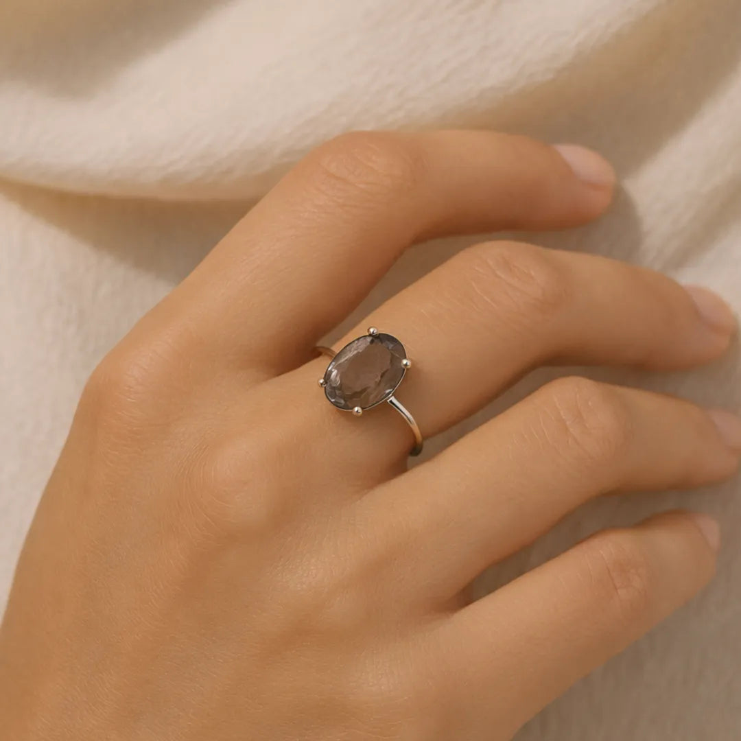 Hand wearing a ring with a smoky topaz stone on a neutral background
