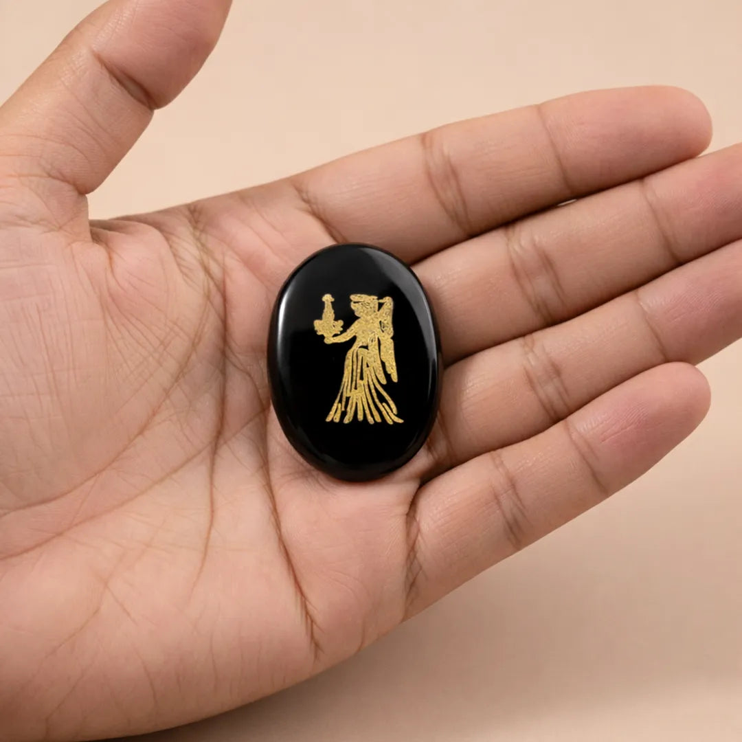 Black stone with gold engraving held in a hand against a beige background
