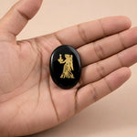 Black stone with gold engraving held in a hand against a beige background