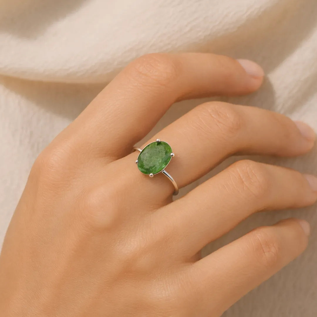 Hand wearing a green gemstone ring on a neutral background