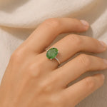 Hand wearing a green gemstone ring on a neutral background