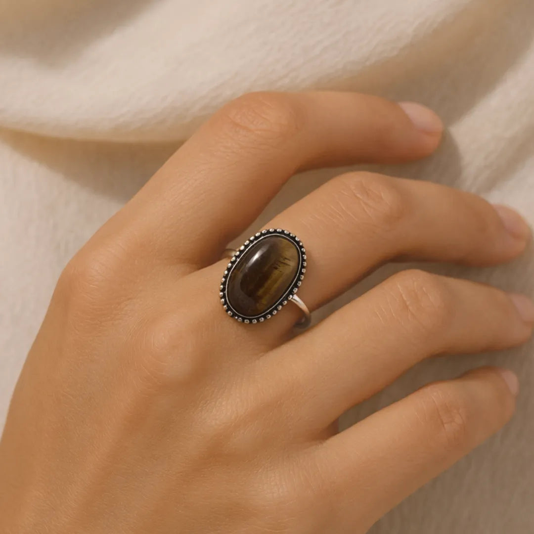 Hand wearing a ring with a tiger's eye stone on a neutral backgroundTiger Eye Ring: Enhances Focus and Decision-Making