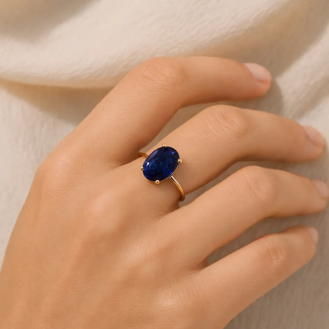 Hand wearing a ring with a blue gemstone on a neutral background