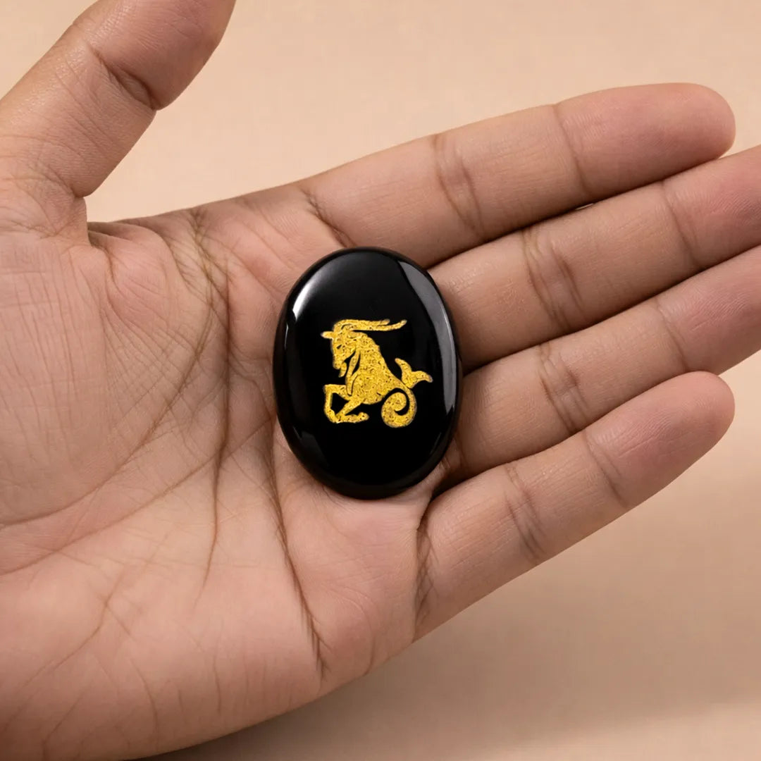 Black stone with a gold dragon design held in a hand against a beige background