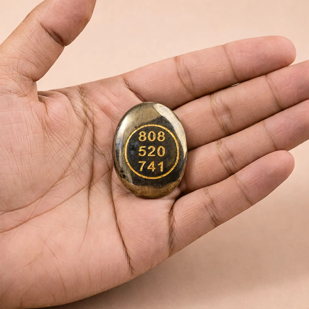 Hand holding a small stone with engraved numbers on a beige backgroundPyrite Zibu Coin – Abhimantrit for Wealth Protection