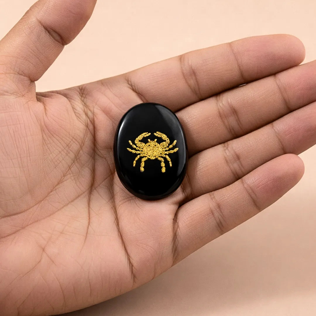 Black stone with a gold crab design held in a hand against a beige background