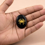 Black stone with a gold crab design held in a hand against a beige background