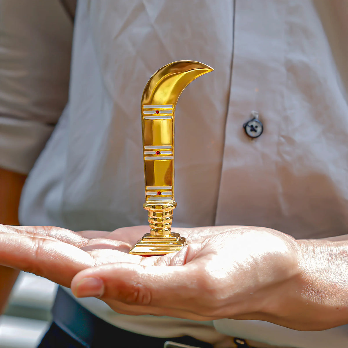Gold curved object held in a hand with a blurred background
