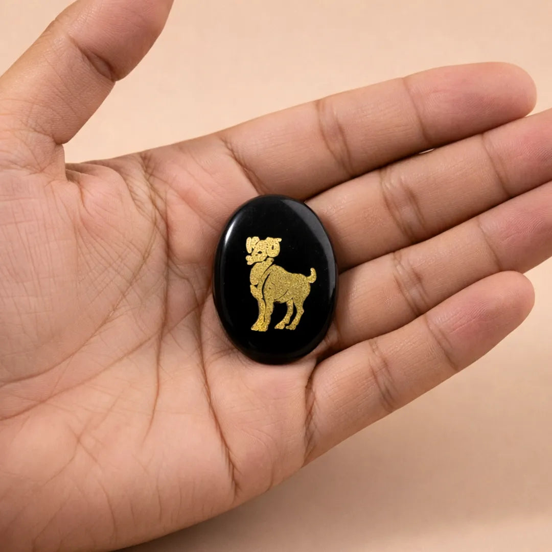 Black stone with gold dog engraving held in a hand against a beige backgroundAries Zodiac Sign Coin – Abhimantrit Astrology Coin for Courage & Energy