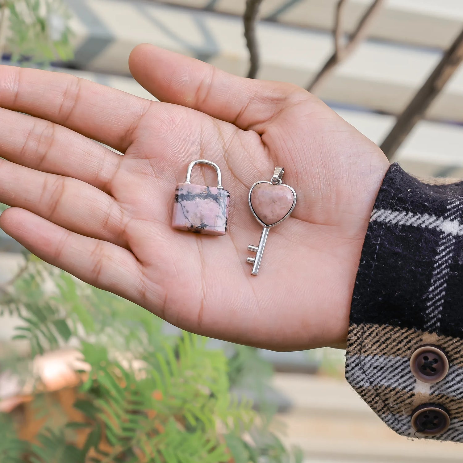 Hand holding a small pink lock and key charm against a blurred outdoor background