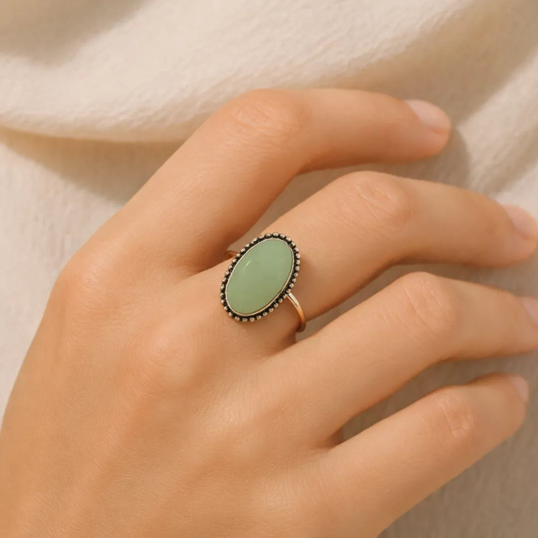 Hand wearing a ring with a green gemstone on a neutral backgroundGreen Aventurine Oval Ring: Attracts Luck and Prosperity