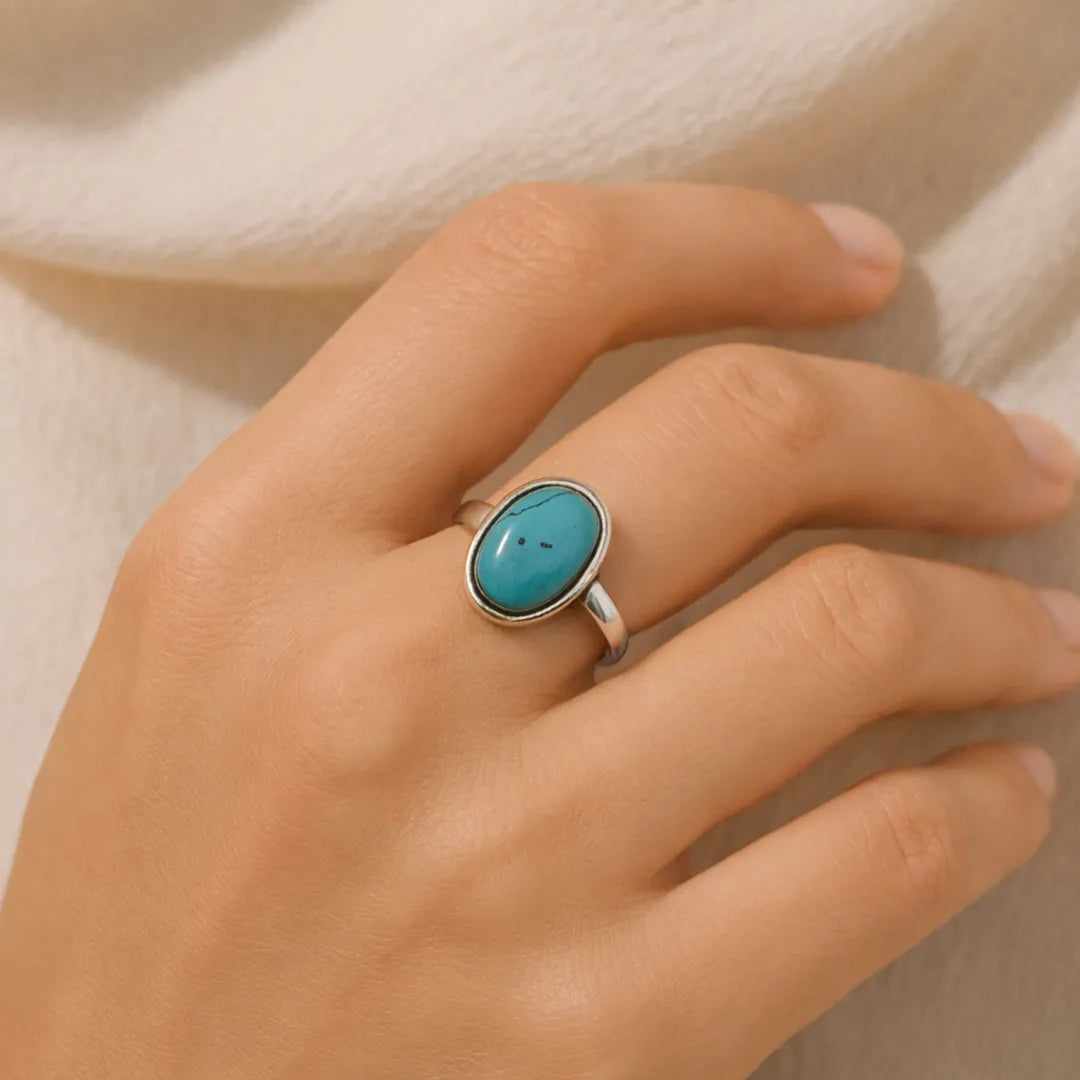Hand wearing a turquoise ring on a neutral background