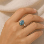 Hand wearing a ring with a blue gemstone on a neutral background