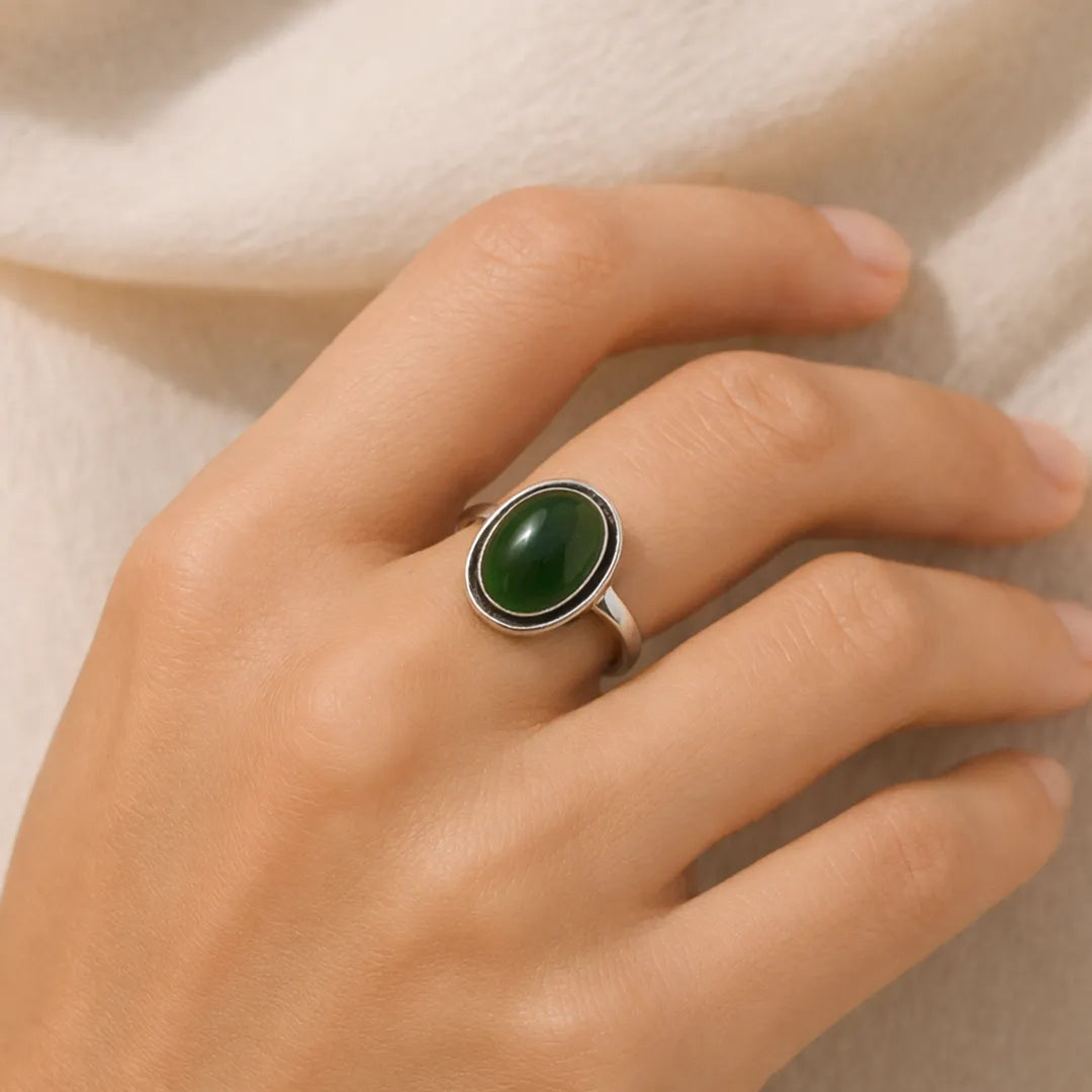 Hand wearing a ring with a green stone on a neutral background