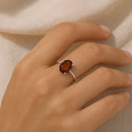 Hand wearing a ring with a brown gemstone on a neutral background