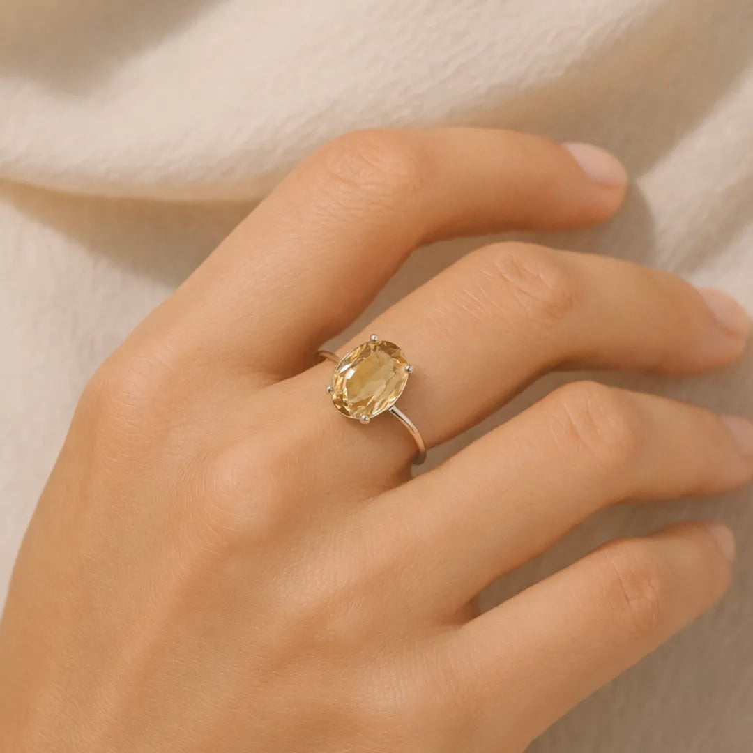 Hand wearing a ring with a yellow gemstone on a neutral background