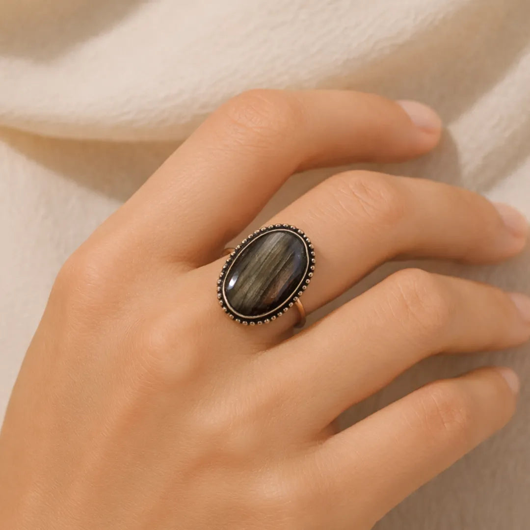 Hand wearing a ring with a dark stone on a neutral background