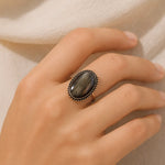 Hand wearing a ring with a dark stone on a neutral background