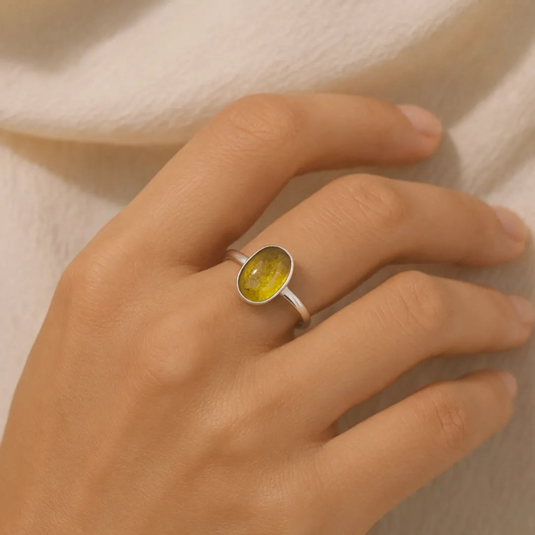 Hand wearing a ring with a yellow stone on a beige background