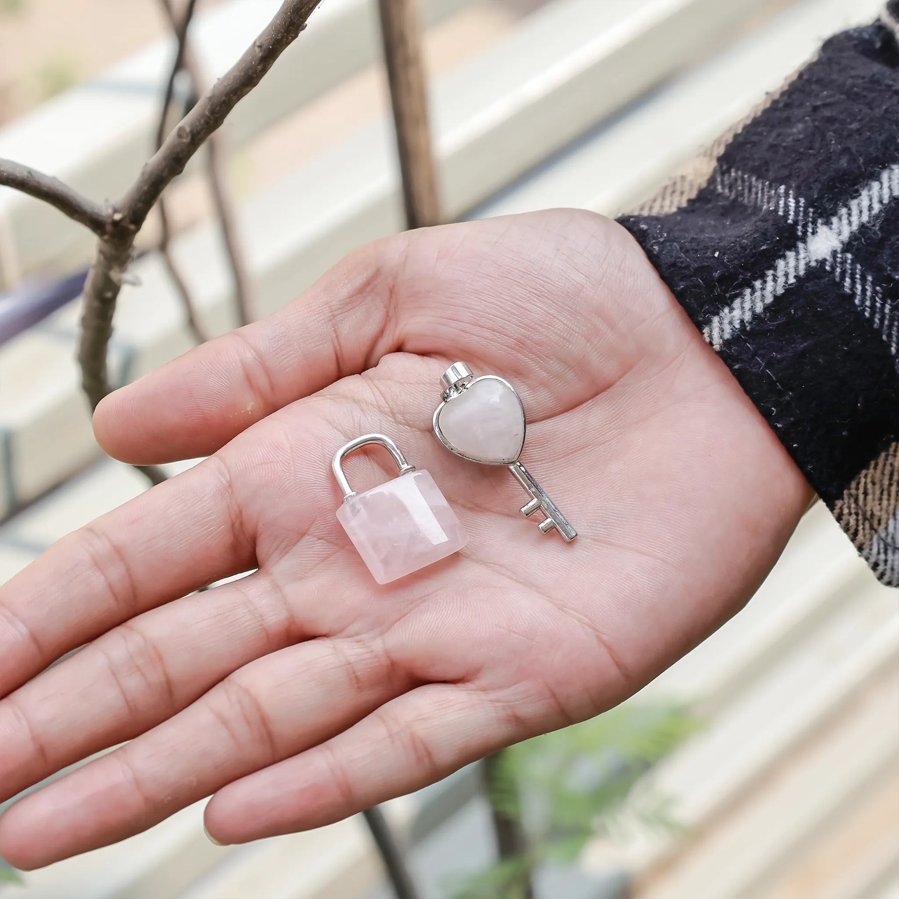 Small pink lock and key held in a hand with a blurred outdoor backgroundRose Quartz Lock And Key Pendant - Abhimantrit & Certified