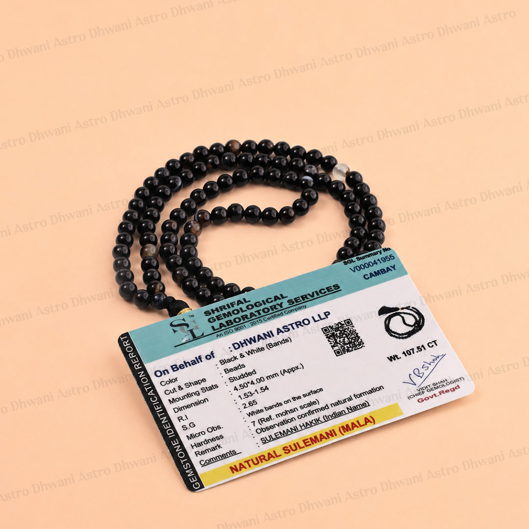 A black beaded necklace with a white accent bead, displayed next to its official authenticity card.