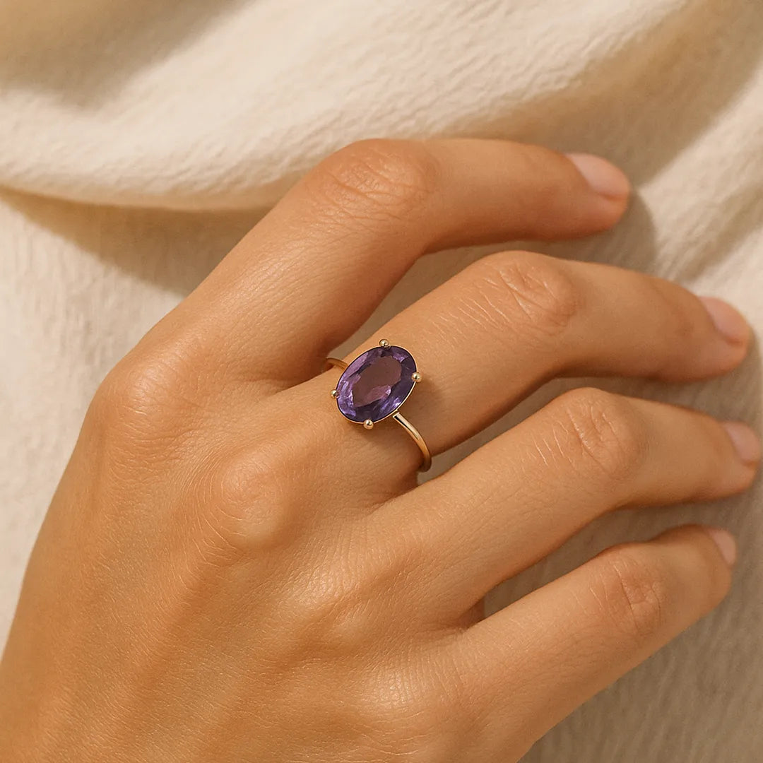Hand wearing a ring with a purple gemstone on a neutral backgroundAmethyst Ring: Attract Luck, Enhance Intuition, Improve Health & Skin