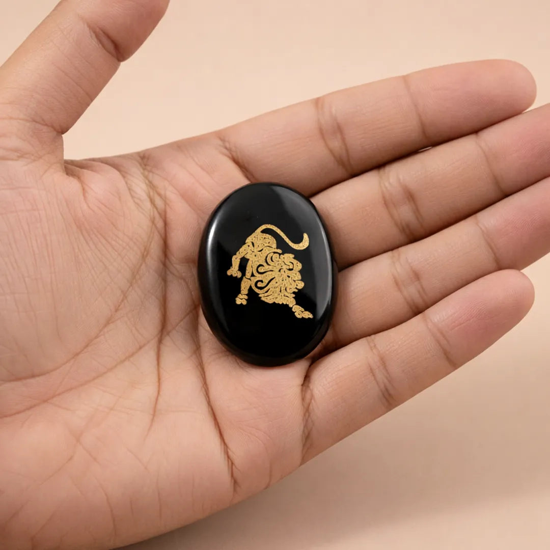 Black stone with gold lion design held in a hand against a beige background