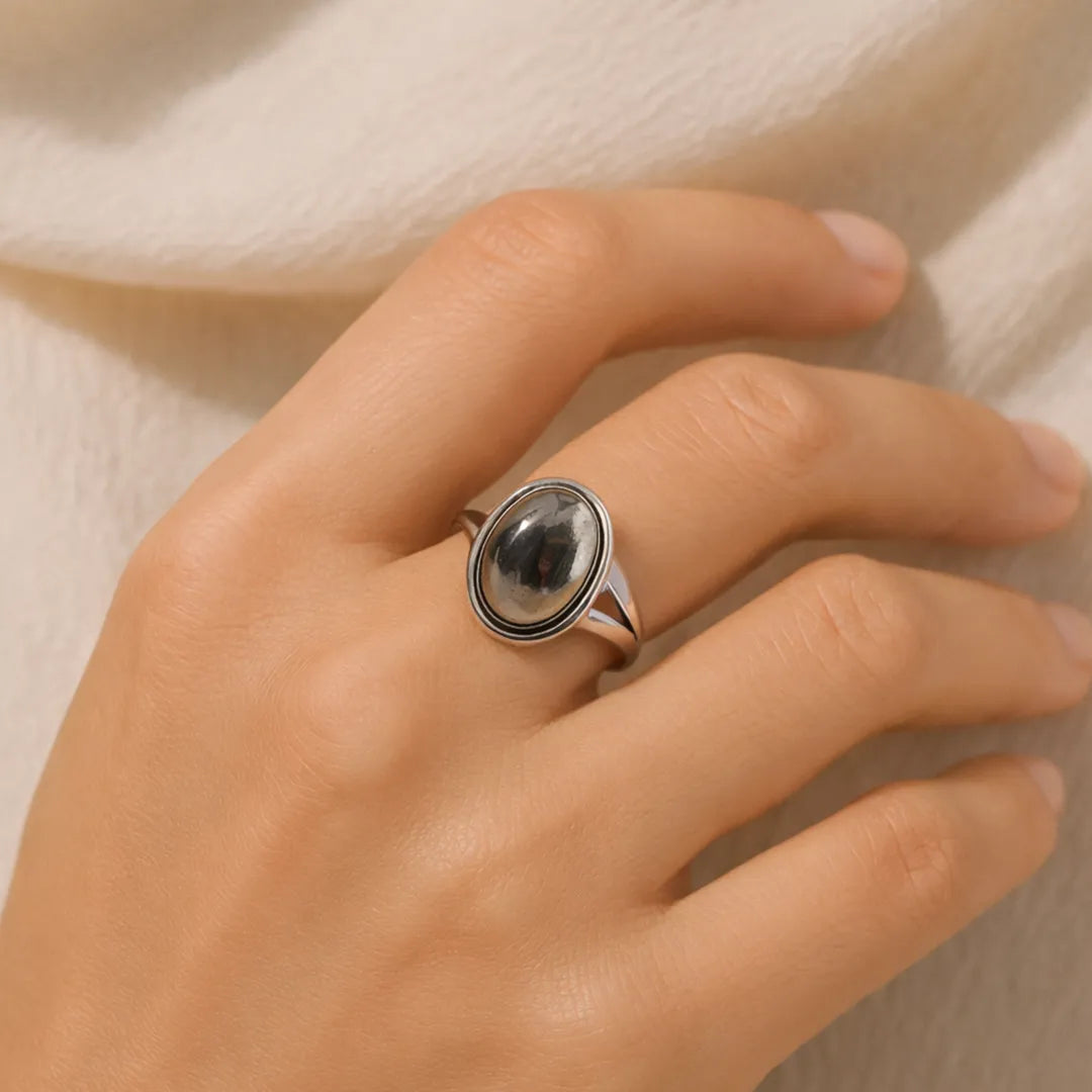 Hand wearing a silver ring with a dark stone on a neutral backgroundPyrite Ring: Attracts Wealth and Abundance
