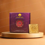 A purple Dhwani Astro box with a red and gold chakra design stands next to a saraswati yantra on a round beige pedestal against a warm brown background.