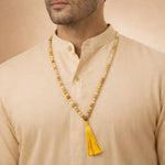 Man wearing a beige kurta with a long beaded necklace featuring a yellow tassel.